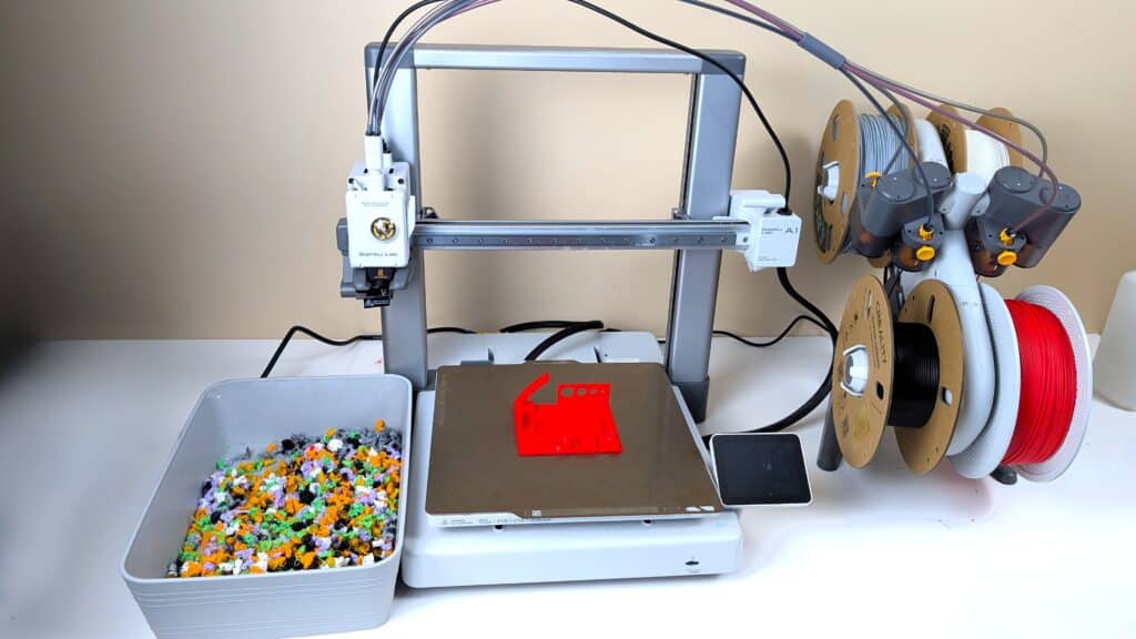 A bambu lab a1 3d printer with ams lite unit and a red torture test printed in pla on the build plate