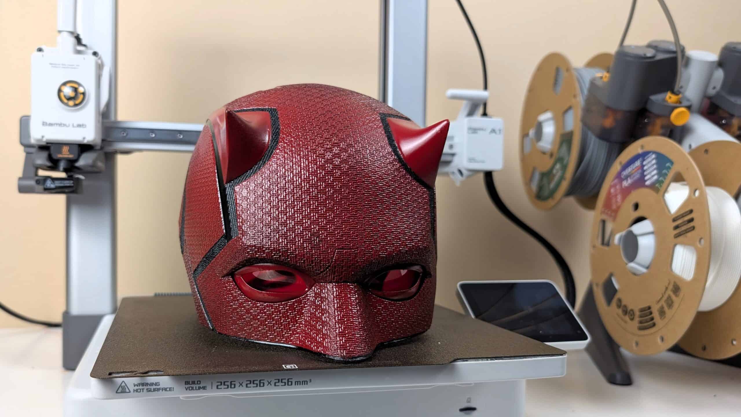 A close up of a 3d printed cosplay daredevil born again helmet on a bambu lab a1 with the ams lite in the background