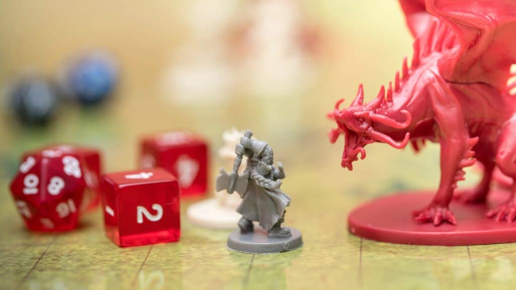 Close up of 3D printed dungeons and dragons miniatures. There is a gray resin soldier fighting a large red dragon with red transparent dice in the background
